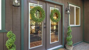 A wooden building with two glass doors, each adorned with a green wreath. There are two small potted plants on the ground. - Nana’s Cozy Cottage in Long Barn – Gated Mountain Retreat (Mi-Wuk Village)
