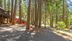 A forested campground with a paved parking area, a red building with a porch, and tall trees. - Nana’s Cozy Cottage in Long Barn – Gated Mountain Retreat (Mi-Wuk Village)