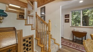 A wooden staircase with a handrail, a wall-mounted light fixture, and a window with a view of trees. - Nana’s Cozy Cottage in Long Barn – Gated Mountain Retreat (Mi-Wuk Village)