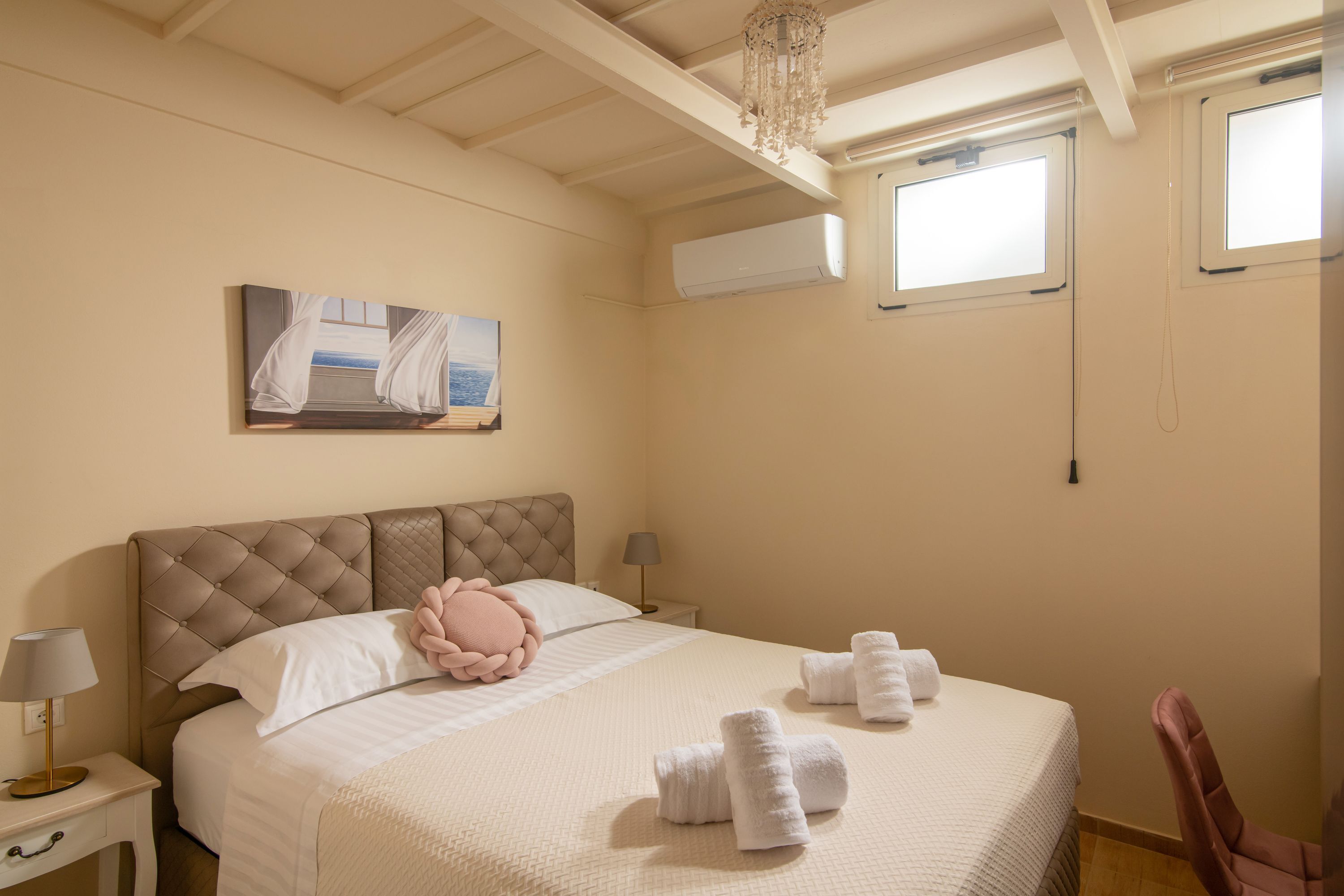 A bedroom with a large bed, a nightstand, a lamp, a painting, and a window.