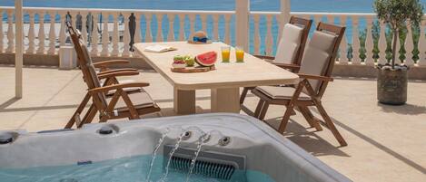 Un jacuzzi con agua en movimiento, una mesa con frutas y bebidas, y vista al mar.