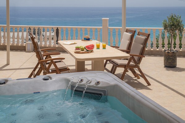 Un bain à remous avec de l’eau en circulation, une table garnie de fruits et de boissons, et une vue sur la mer.