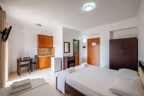 A hotel room with a bed, a desk, a refrigerator, and wooden cabinets. - La Luna Resort (Ksamil)