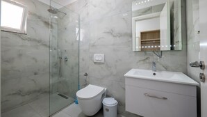 Une salle de bain avec une douche à parois de verre, des toilettes, un lavabo et un miroir avec éclairage intégré.