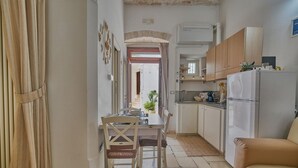 Een kleine keuken met een eettafel, stoelen, een koelkast en een bank.