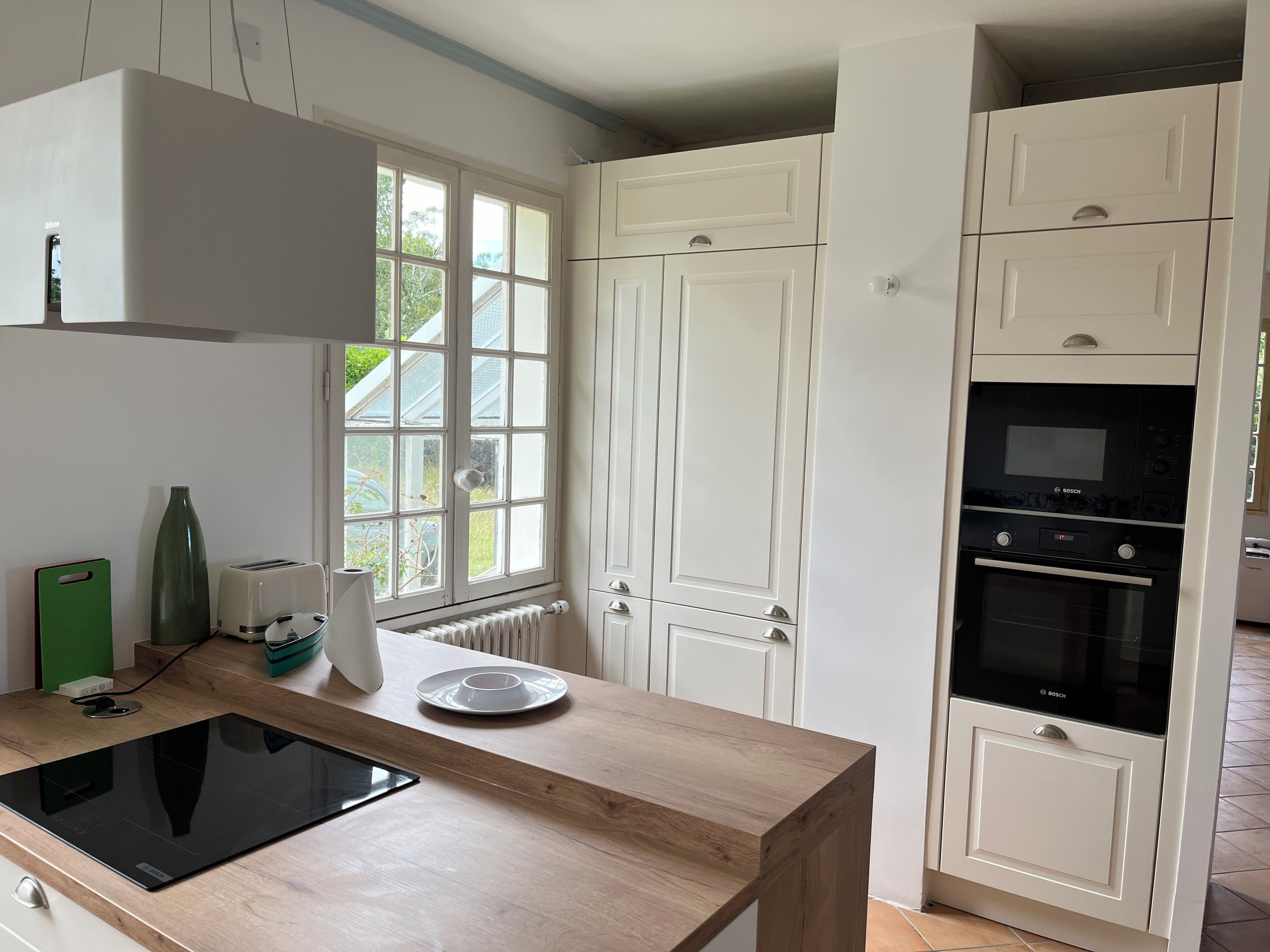 A kitchen with a built-in stove, a window, and white cabinets.