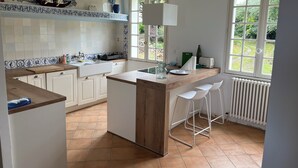 A kitchen with a central island, white cabinets, blue and white tiles, and a view of greenery outside. - Family house with sea view / Beach 10min walk (Ploubazlanec)