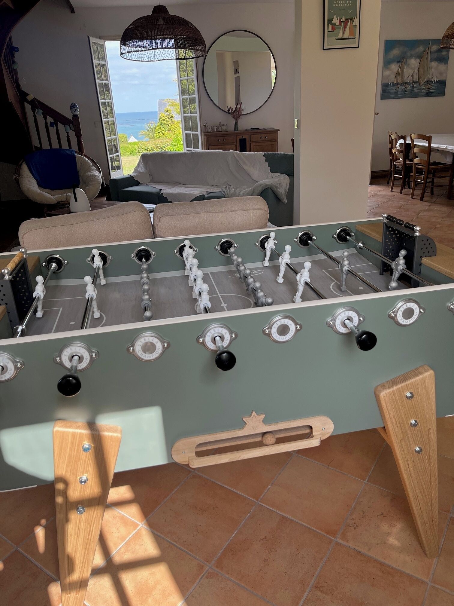A foosball table in a room with a view of the ocean, a sofa, and a dining area.