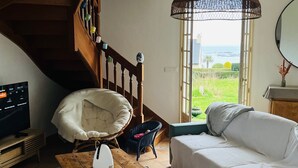 A living room with a wooden staircase, a white sofa, a wicker chair, a wooden coffee table, and a television. - Family house with sea view / Beach 10min walk (Ploubazlanec)