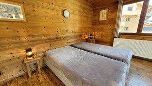 Una habitación de cabaña de madera con dos camas, una mesita con una lámpara, un reloj y cuadros en las paredes.