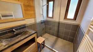 Un baño moderno con ducha, tocador de madera y un taburete pequeño.