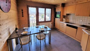 Un interior de madera con una mesa de comedor para cuatro, una cocina con armarios de madera y un gran reloj de pared.
