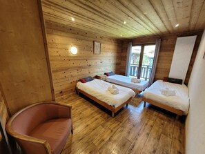 Ein Zimmer einer Holzhütte mit drei Betten, einem Stuhl und einem Fenster.