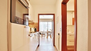 Un pasillo estrecho con una cocina a la izquierda, una zona de comedor con mesa y sillas en el centro, y un baño a la derecha.
