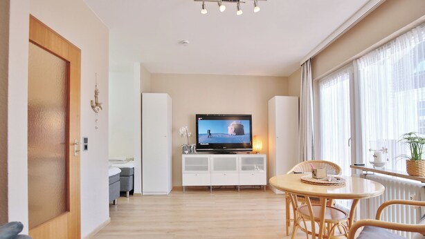 Una sala de estar moderna con televisor, mesa de comedor y sillas de mimbre.