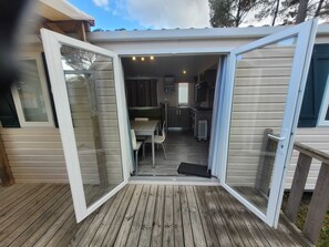 A covered outdoor area with a table and chairs, a small kitchen, and a sliding glass door. - Mobile home at a campground (Lit-et-Mixe)