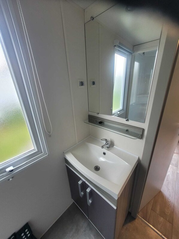 A small bathroom with a white sink, a mirror, and a window. - Mobile home at a campground (Lit-et-Mixe)