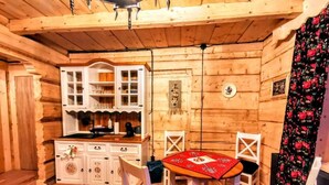 A wooden cabin interior with a dining table, chairs, a cabinet with glass doors, and a hanging decoration.