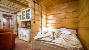 A wooden cabin room with a bed, a small table, a lamp, and a cabinet.