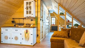 A cozy attic room with a wooden ceiling, a white cabinet with glass doors, a brown sofa, and a staircase leading to another level.