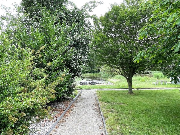 Stroll through lush greenery and mature trees along a tranquil pathway leading to a serene body of water.