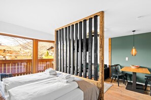 Quarto com duas camas, divisória de madeira, mesa de jantar com cadeiras e vista para o exterior.
