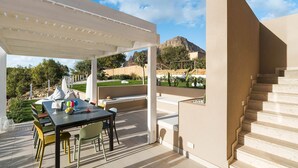 Eine Terrasse im Freien mit Tisch und Stühlen, einem überdachten Bereich und Blick auf eine Berglandschaft.
