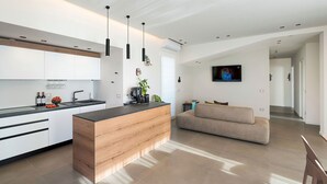 Eine moderne Küche mit einer zentralen Kochinsel, einem Sofa und einem Fernseher im Wohnbereich.