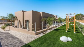Ein modernes Gebäude mit beiger Fassade, einem verschlossenen Eingangsbereich und einem kleinen Garten mit Kunstgrasanlage und weißen, kugelförmigen Objekten.