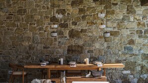 A rustic dining area with a stone wall backdrop, wooden table, and hanging pendant lights.
