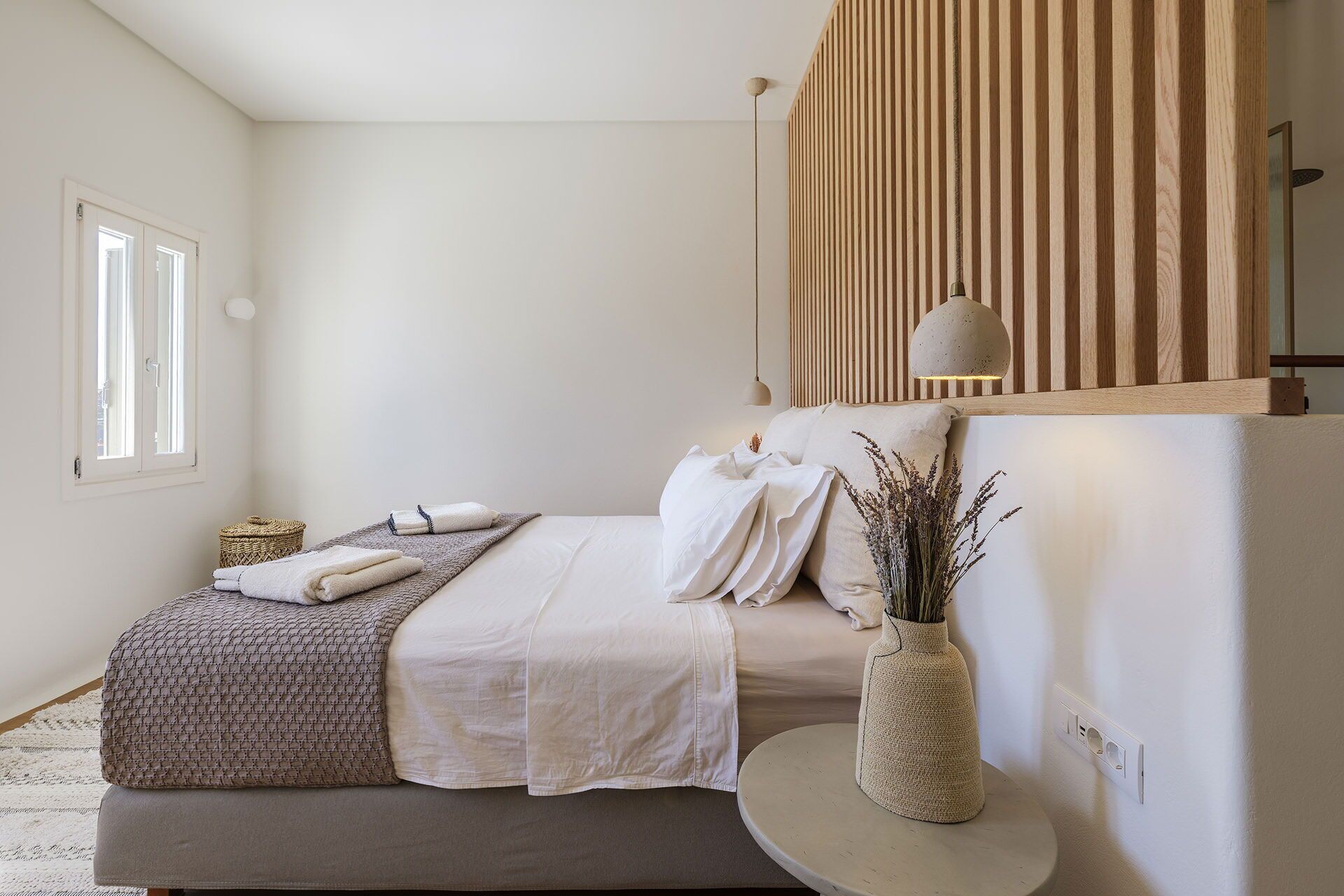 A minimalist bedroom with a bed, bedside table, and a wall-mounted light fixture.
