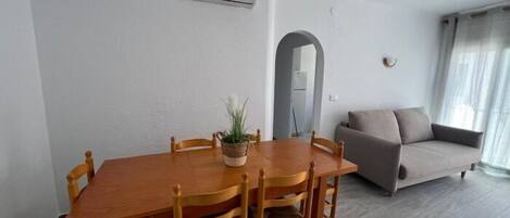 Un comedor con una mesa y sillas de madera, un sofá gris y un equipo de aire acondicionado en la pared.