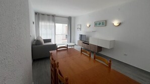Ein modernes Wohnzimmer mit einer Couch, einem Esstisch mit Stühlen, einem Fernseher und einem kleinen Balkon.
