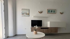 Ein modernes Wohnzimmer mit Flachbildfernseher, einem kleinen runden Tisch mit Pflanze und Kunstwerk an der Wand.