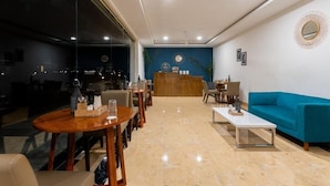 A modern hotel lobby with a reception desk, seating area, and a large window offering a view of the cityscape.