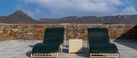 Two lounge chairs with a stone wall and a mountain view in the background.