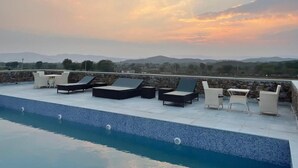 A rooftop pool with lounge chairs and a view of distant mountains.