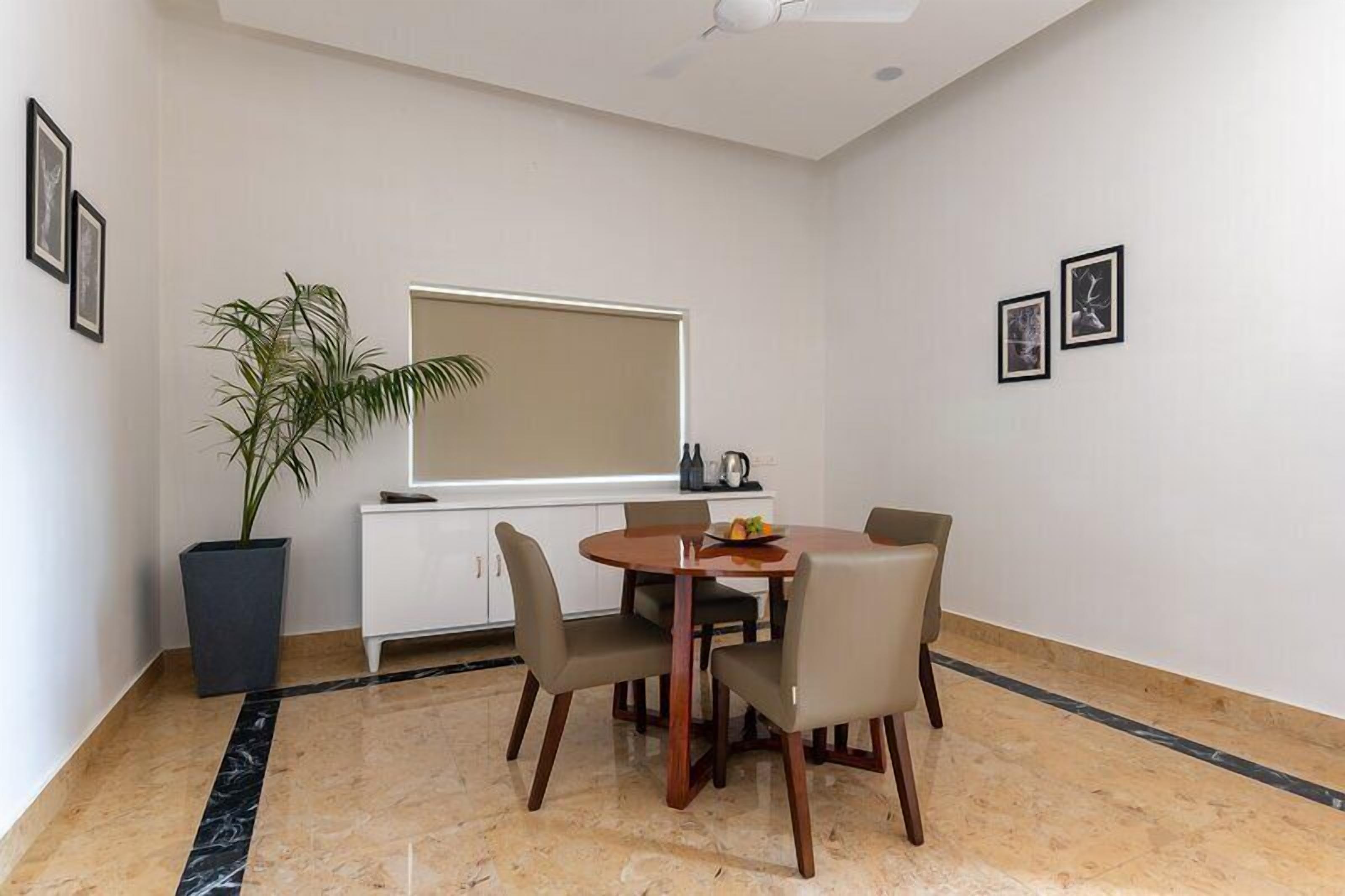 Uma área de refeições com uma mesa redonda, quatro cadeiras, um vaso de planta, uma janela e um armário branco.