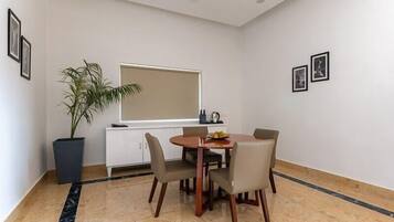 Uma área de refeições com uma mesa redonda, quatro cadeiras, um vaso de planta, uma janela e um armário branco.