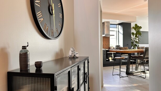 A modern kitchen with a dining area, featuring a large wall clock, a cabinet with glass doors, and a potted plant. - Stylish Freemans Bay Stay (Auckland)