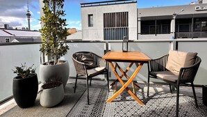 A rooftop terrace with a table and chairs, potted plants, and a view of a city skyline including a tower. - Stylish Freemans Bay Stay (Auckland)