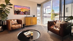 A modern living room with leather sofas, a coffee table, and a large window offering a city view. - Stylish Freemans Bay Stay (Auckland)