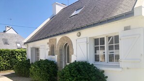Una casa blanca con techo de tejas grises, dos contraventanas blancas y una ventana pequeña.