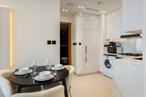 A modern kitchen with a built-in washer and dryer, a dining area with a table set for four, and a small seating area.