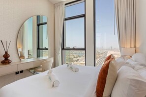 A hotel room with a large bed, a desk, a mirror, and a view of a cityscape.
