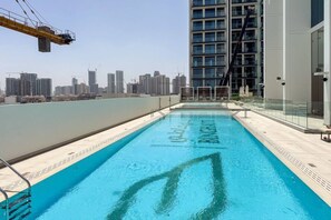 A rooftop swimming pool with a city skyline view, surrounded by high-rise buildings and construction cranes.