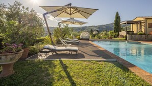 Ein Poolbereich mit Liegestühlen, Sonnenschirmen und Blick auf die umliegende Landschaft.