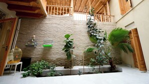 A spacious indoor area with a high wooden ceiling, stone walls, and a variety of potted plants. - AIST HOTEL (Bukhara)