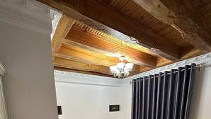 A bedroom with a wooden ceiling, a bed with white linens, a nightstand, and a dark curtain. - AIST HOTEL (Bukhara)