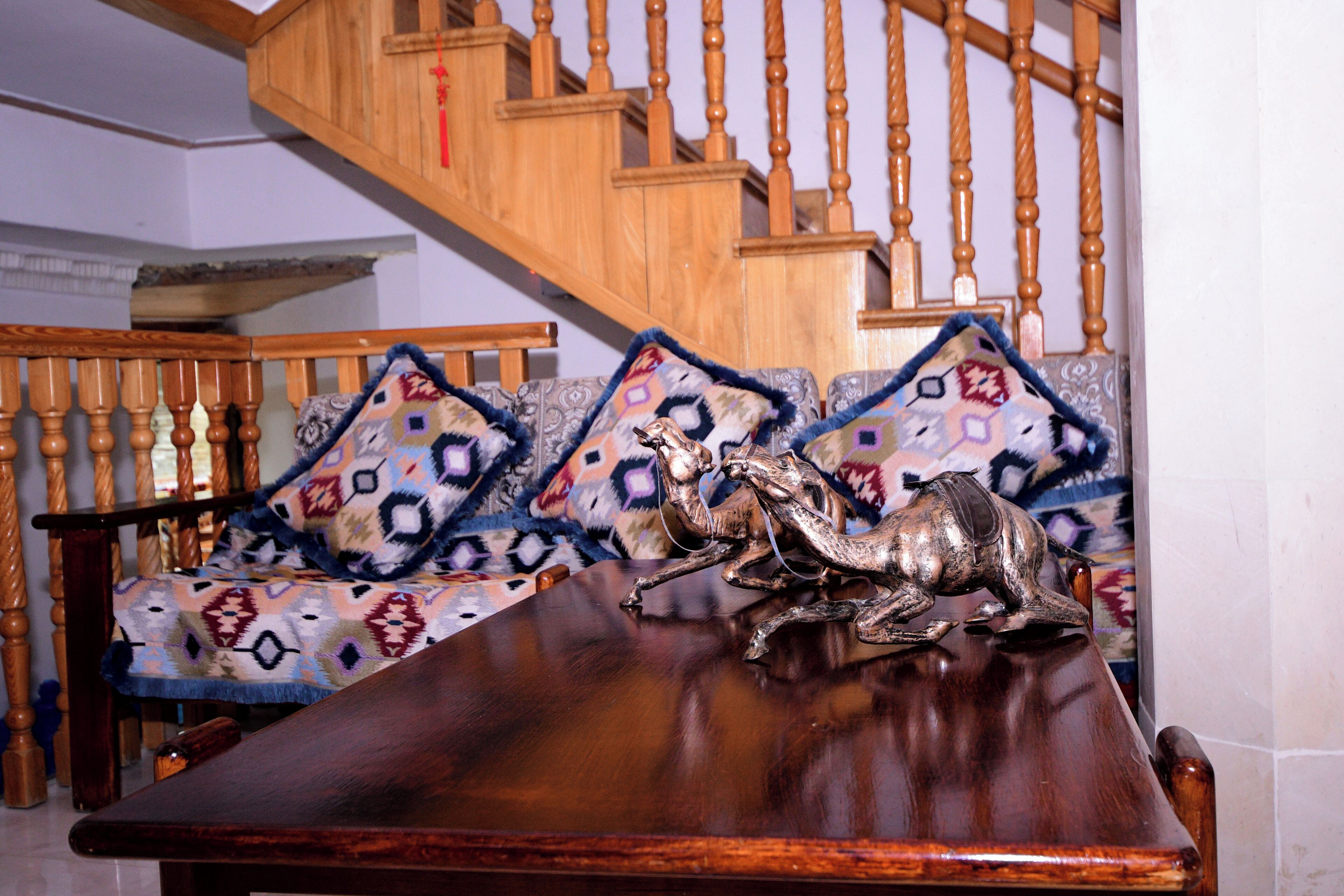A wooden staircase with a railing, a patterned sofa with cushions, and a wooden table with a horse sculpture.